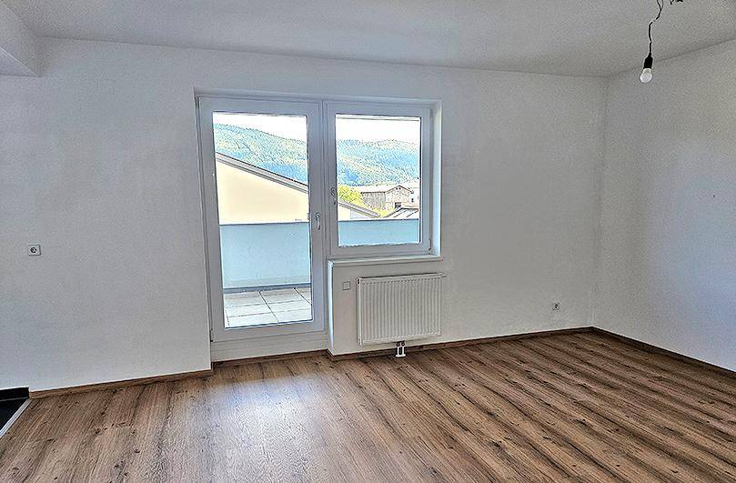 Heller Raum mit Laminatboden und Zugang zu einem Balkon mit Bergblick.