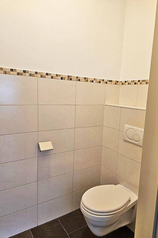 Kleines Gäste-WC mit Wand-WC und hellen Fliesen an den Wänden, in gutem Zustand.