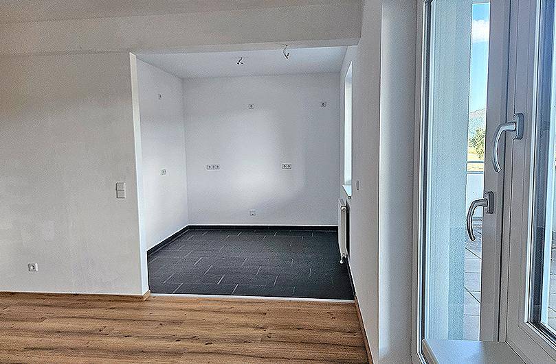 Übergangsbereich mit Laminat- und Fliesenboden, hell durch die Balkontür und Fenster.