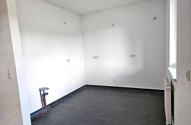 Leere Küche mit Fliesenboden und sichtbaren Anschlüssen für Spüle und Geräte.