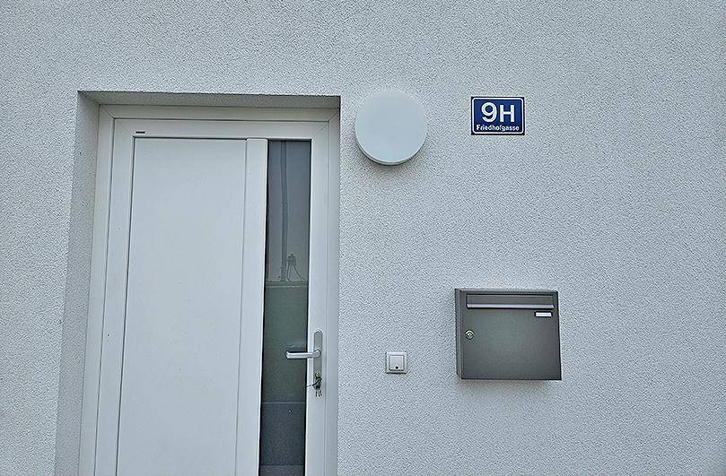 Weiße Hausfassade mit Eingangstür, Briefkasten und Hausnummernschild.