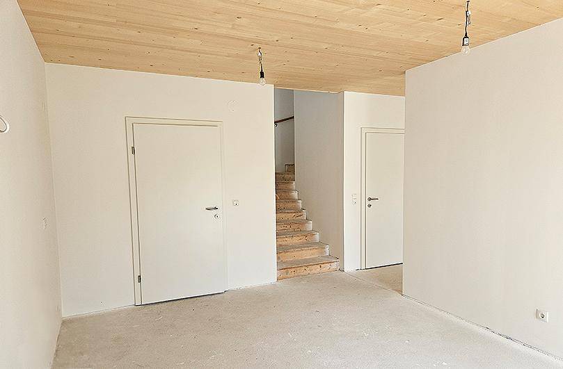 Großer, heller Raum mit Holzdecke, mehreren Türen und einer sichtbaren Holztreppe.