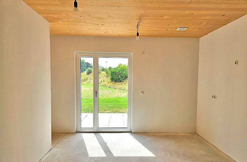 Geräumiger, unmöblierter Wohnbereich mit Holzdecke und direktem Zugang zur Terrasse.