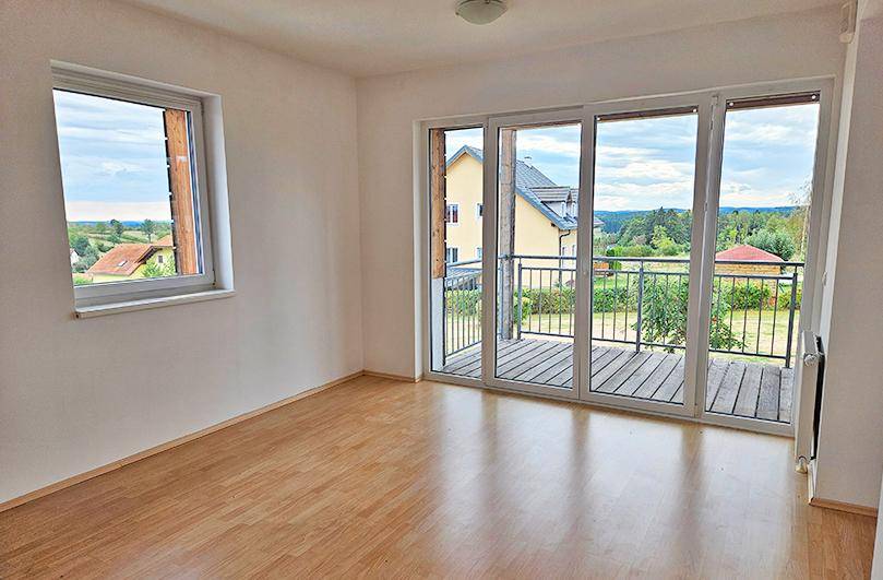 Geräumiges Wohnzimmer mit Laminatboden, großen Fenstern und Zugang zum Balkon mit Weitblick.