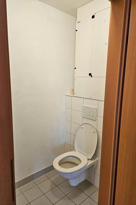 Separate Toilette mit Wand-WC und hellen Fliesen, in einem funktionalen Design.