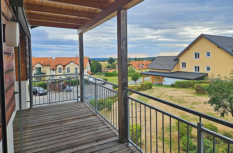 Geräumiger Balkon mit Holzbelag und Metallgeländer, bietet Blick auf die Nachbarschaft.