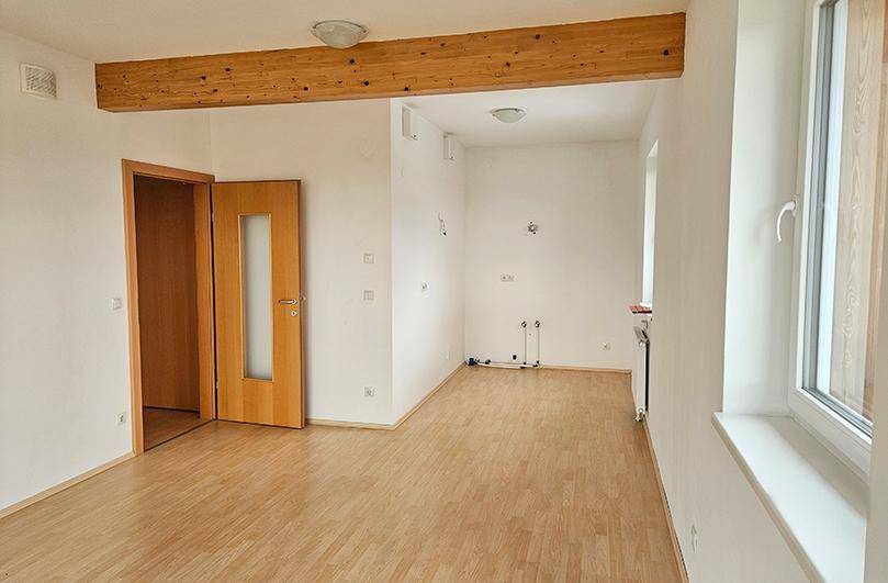 Heller Raum, vorbereitet für eine Küche, mit sichtbarem Holzbalken und Fenster.