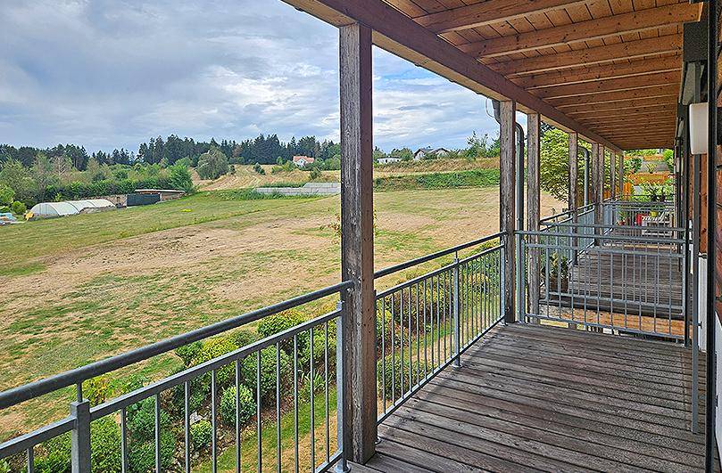 Langer Balkon mit Holzboden und weitem Blick über grüne Felder und die Umgebung.