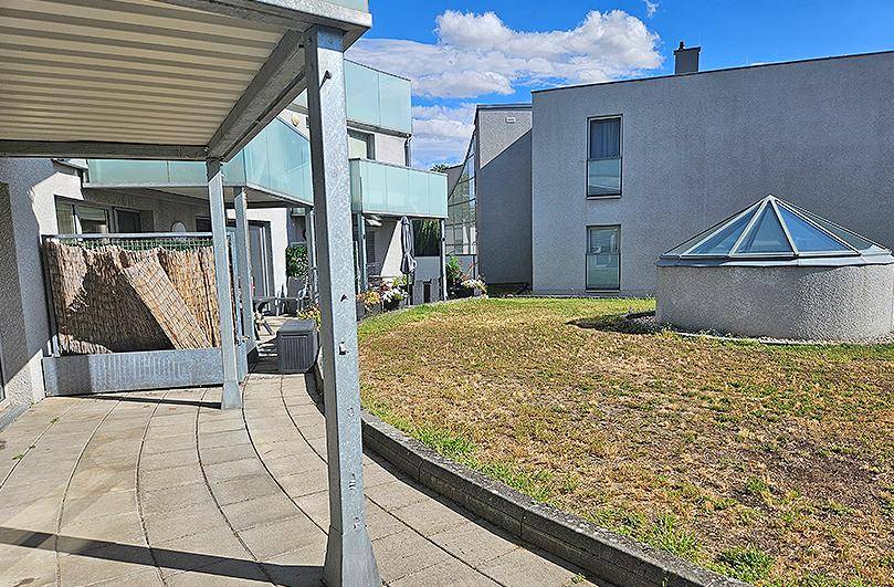 Außenbereich mit gepflasterter Terrasse, Rasenfläche und moderner Architektur im Hintergrund.