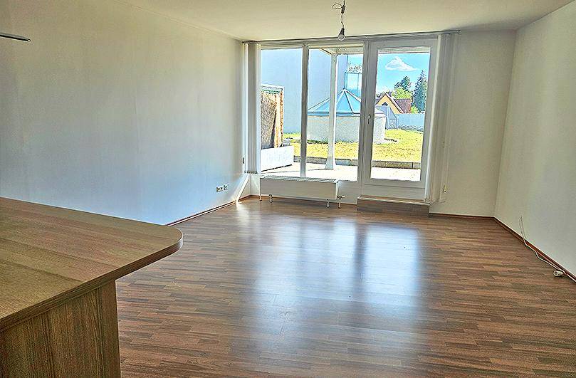 Helles Wohnzimmer mit Laminatboden und großen Glasfronten zum Außenbereich.
