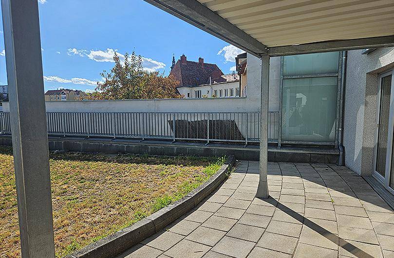 Große gepflasterte Terrasse mit Rasenfläche und Blick auf die umliegenden Gebäude.