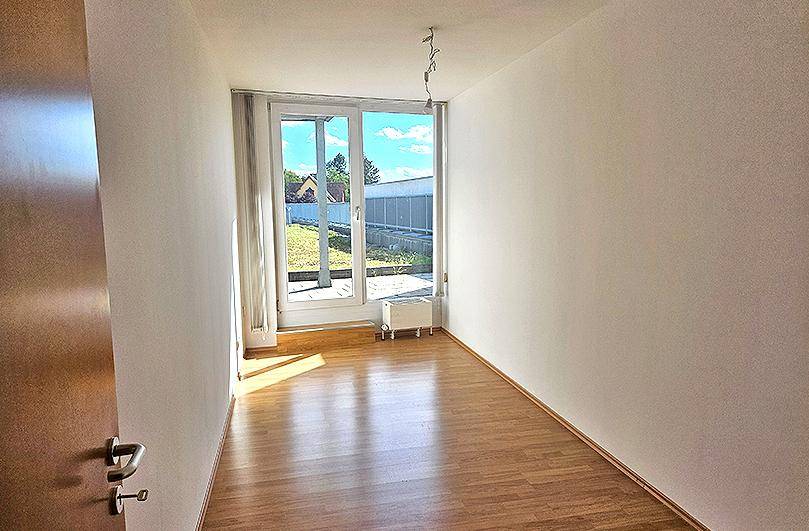 Lichtdurchflutetes Zimmer mit Laminatboden und großen Fenstern zum Außenbereich.