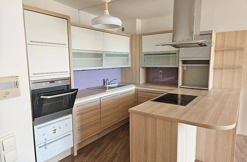 Moderne Einbauküche mit hellen Holzfronten, Induktionskochfeld auf der Insel und lila Spritzschutz.
