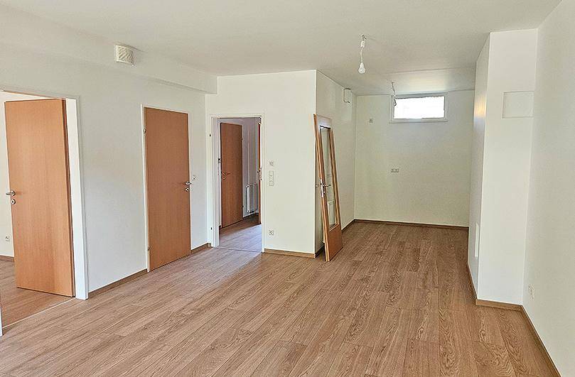 Geräumiges, leeres Wohnzimmer mit Holzboden und mehreren Türen, bereit zur Einrichtung.