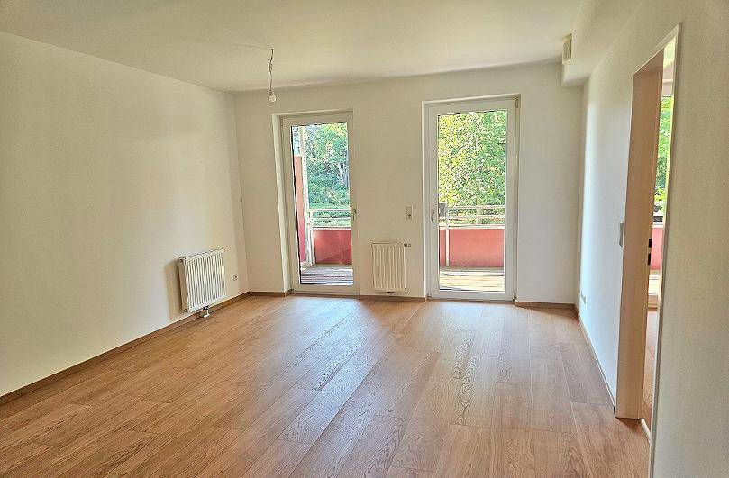 Helles Zimmer mit Holzboden, zwei Balkontüren und Heizkörpern, ideal für Wohn- oder Schlafbereich.