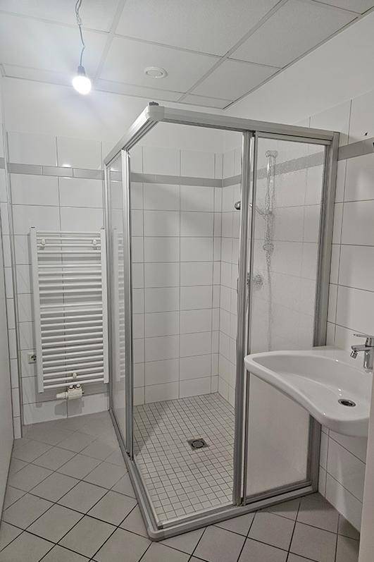 Badezimmer mit Duschkabine, Waschbecken und beheiztem Handtuchhalter, komplett gefliest.