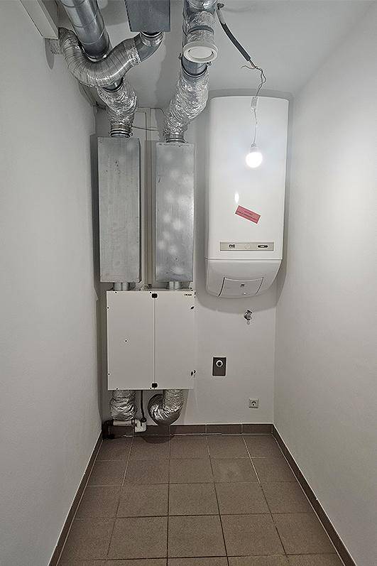 Technikraum mit sichtbaren Rohren, Lüftungskanälen und einem Warmwasserbereiter.