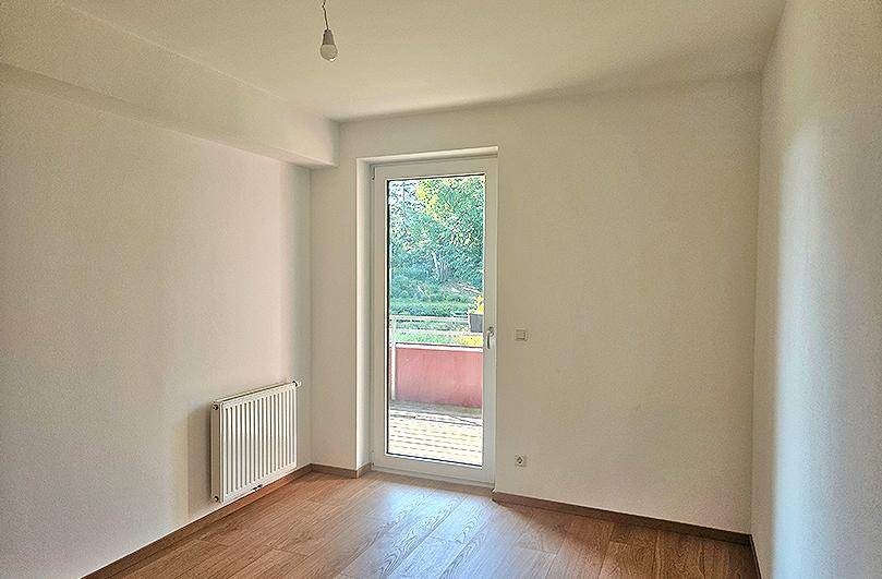 Ruhiges Schlafzimmer mit Holzboden, Zugang zum Balkon und einem Heizkörper.