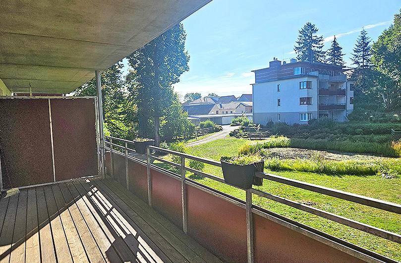 Sonniger Balkon mit Holzboden und weitem Blick über eine grüne Wohngegend.