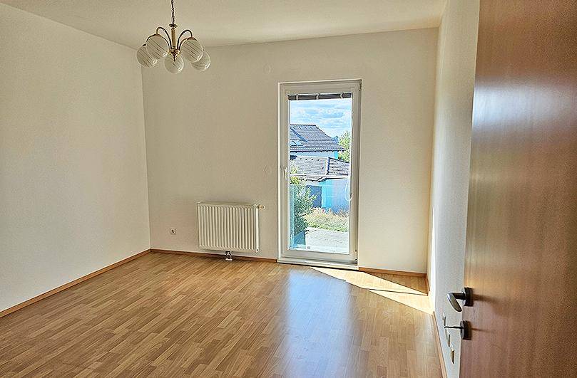 Freundliches Zimmer mit Parkettboden, Deckenleuchte und Blick ins Grüne.