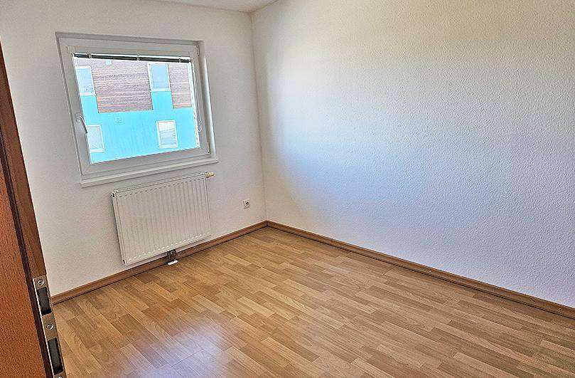 Kleines Zimmer mit Parkettboden, Heizkörper und Fenster mit Blick auf Nachbargebäude.
