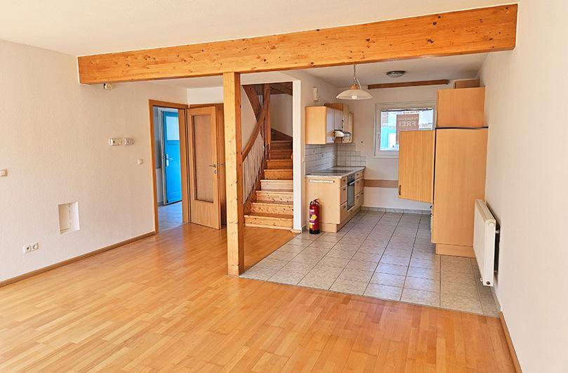 Offener Wohnbereich mit Holzbalken, Parkettboden und integrierter Küche mit Treppenzugang.