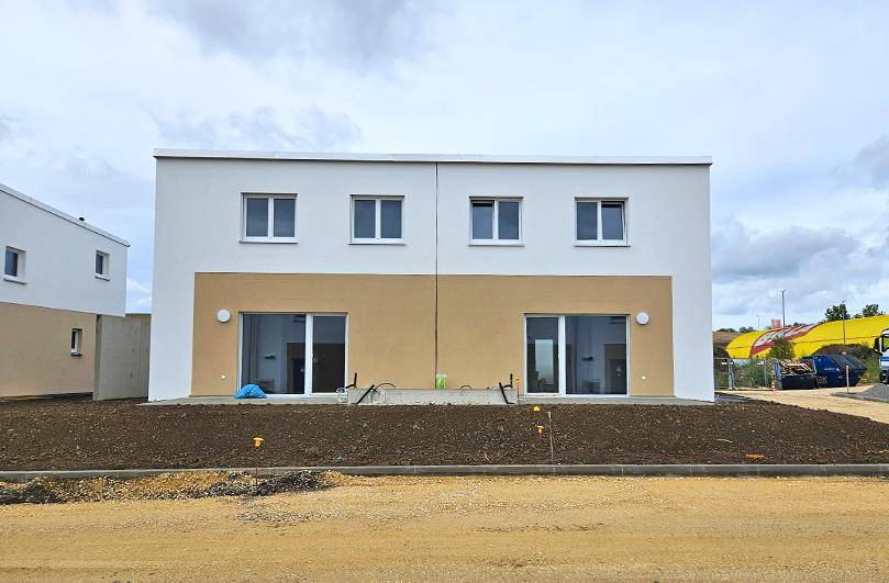 Vorderansicht eines Doppelhauses im Neubaugebiet mit großen Fensterfronten und moderner Gestaltung.