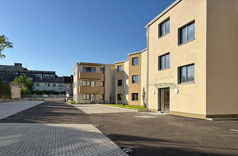 Eingangsbereich eines modernen Wohngebäudes mit beiger Fassade und gepflastertem Parkplatz.