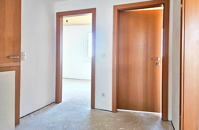 Heller Flur mit zwei Holztüren und unfertigem Betonboden in einem Neubau.