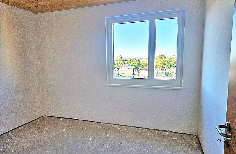 Unfertiges Zimmer mit Holzbalkendecke, weiß gestrichenen Wänden und weitem Ausblick.