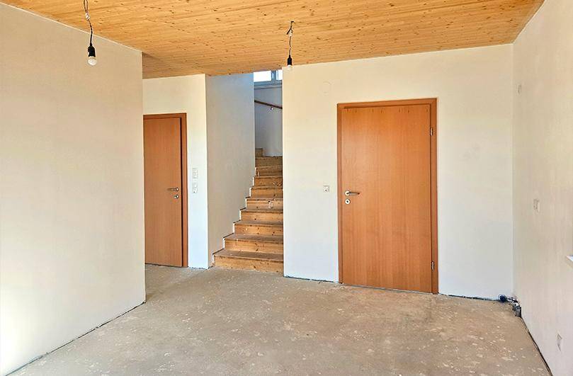Unfertiger Eingangsbereich mit Holztüren, Holztreppe und einer Decke aus Holzpaneelen.