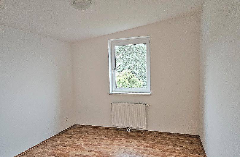 Gemütliches Schlafzimmer mit Laminatboden, einem Fenster und einem Heizkörper unter dem Fenster.