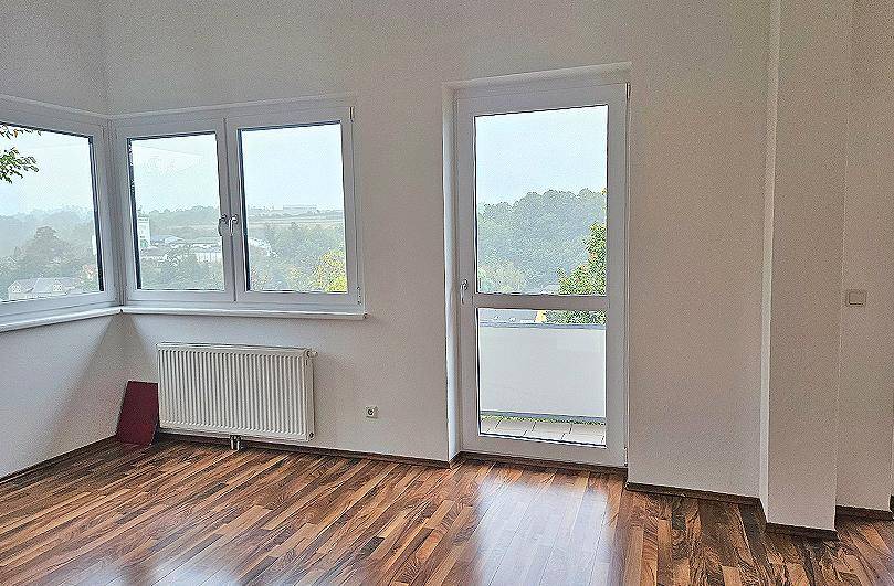 Heller Raum mit Laminatboden, Heizkörper und Fenstern, die einen weiten Blick bieten.