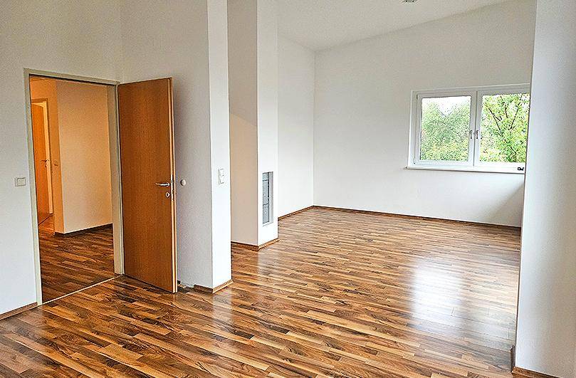 Helles Wohnzimmer mit Laminatboden und einem Fenster, das viel Tageslicht hereinlässt.