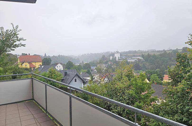 Weiter Blick vom Balkon über eine grüne Landschaft mit Häusern und einem Kirchturm in der Ferne.