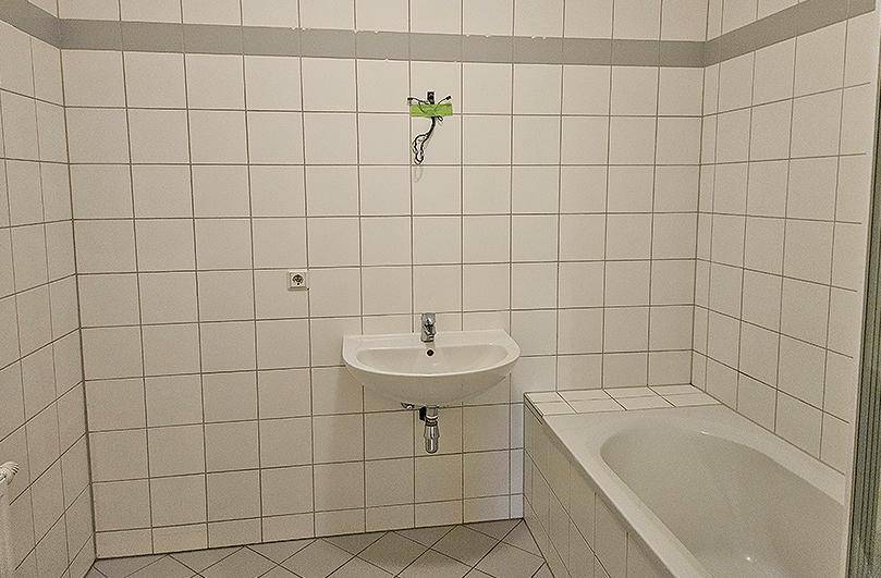 Badezimmer mit weißen Fliesen, einem Waschbecken und einer Badewanne, bereit zur Modernisierung.