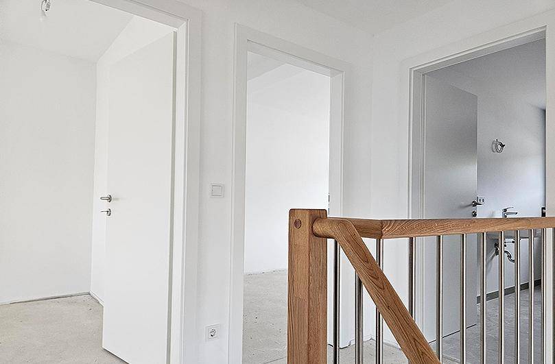 Heller Flur im Obergeschoss mit Holzgeländer und Blick in angrenzende, unfertige Räume.
