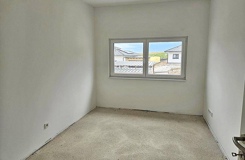 Unfertiges Schlafzimmer mit weiß gestrichenen Wänden und einem Fenster mit Blick ins Grüne.