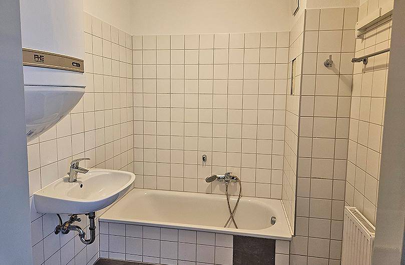 Funktionales Badezimmer mit Badewanne, Waschbecken und weißen Fliesen, inklusive Warmwasserboiler.