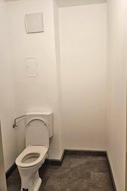 Separates Gäste-WC mit Toilette, dunklem Fliesenboden und einer Wandlüftung.