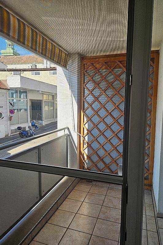Kleiner Balkon mit Fliesenboden, Markise und Blick auf die umliegende Straße.