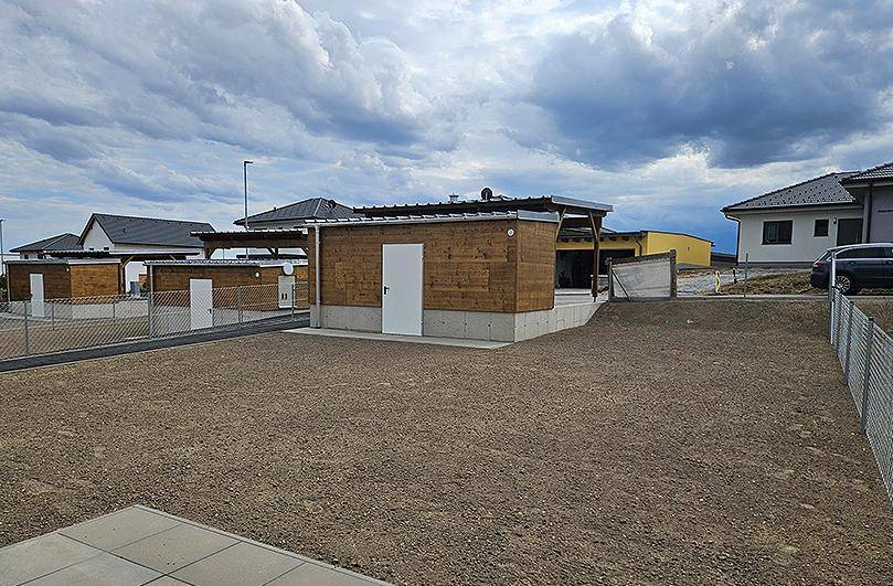 Holzverkleidete Nebengebäude mit Carports und einem vorbereiteten Außenbereich auf Schotter.