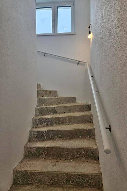 Unfertiges Treppenhaus mit Betonstufen und einem Handlauf in einem Neubau.