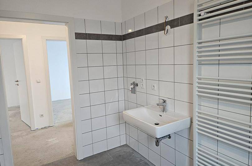 Helles Badezimmer in einem Neubau mit weißen Fliesen, Waschbecken und beheiztem Handtuchhalter.