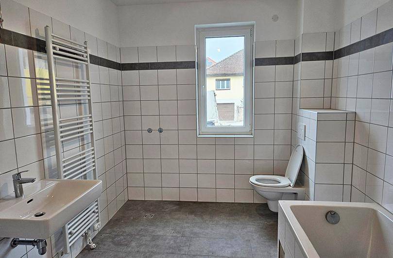 Modernes Badezimmer in einem Neubau mit weißen Fliesen, Badewanne, WC und Fenster.