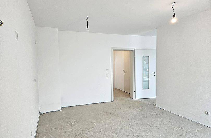 Geräumiger, unfertiger Wohnbereich in einem Neubau mit Rohbetonboden und weißen Wänden.