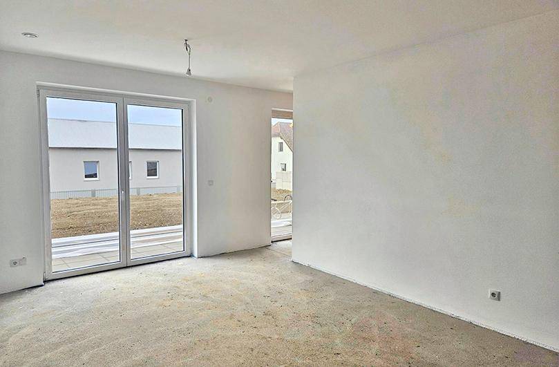 Großer, heller Wohnbereich in einem Neubau mit Schiebetüren zum Garten und Rohbetonboden.