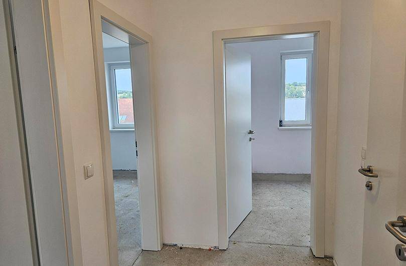 Heller Flur in einem Neubau mit zwei offenen Türen zu weiteren Räumen.