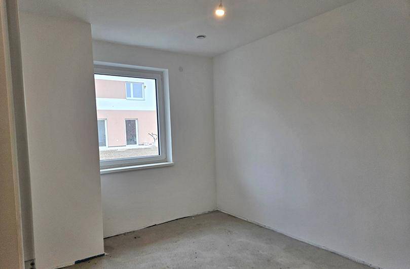 Helles, unfertiges Schlafzimmer in einem Neubau mit einem Fenster und Rohbetonboden.