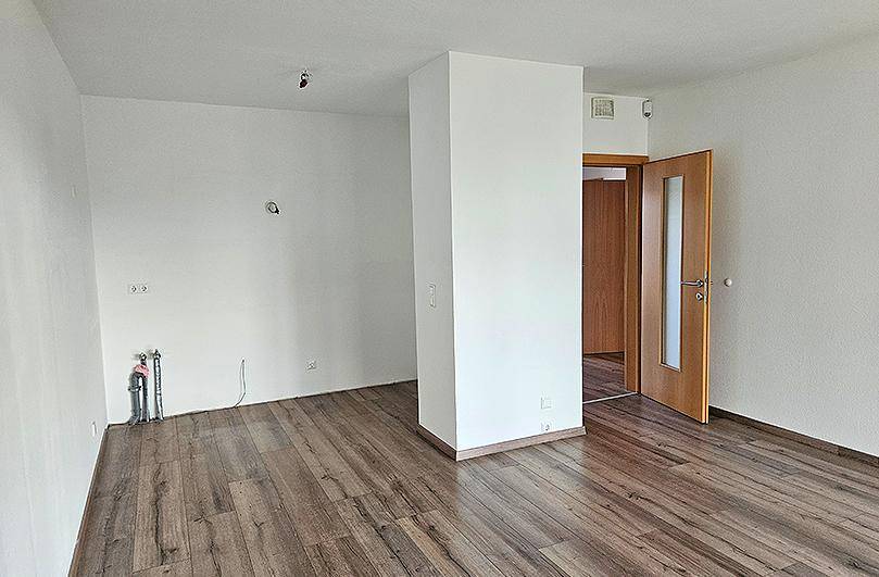 Heller Raum mit Laminatboden und weiß gestrichenen Wänden, bereit für die individuelle Gestaltung.